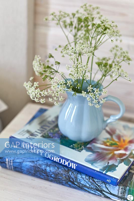 Pichet bleu pâle de fleurs sauvages coupées sur table de chevet avec des livres