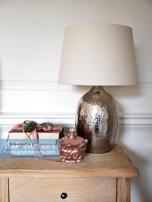 Lampe métallique sur table de chevet avec des livres emballés comme cadeau de Noël