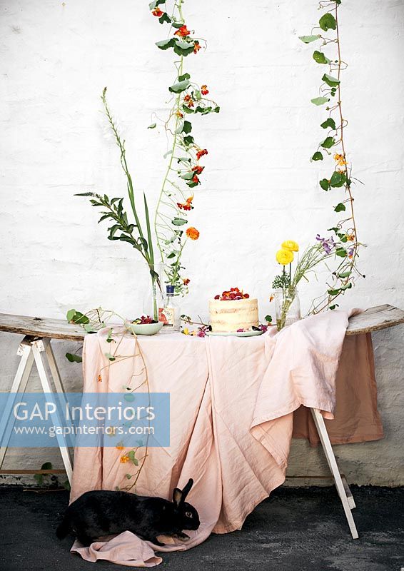 Lapin de compagnie à côté de la table de jardin remplie de fleurs et de nourriture de pique-nique