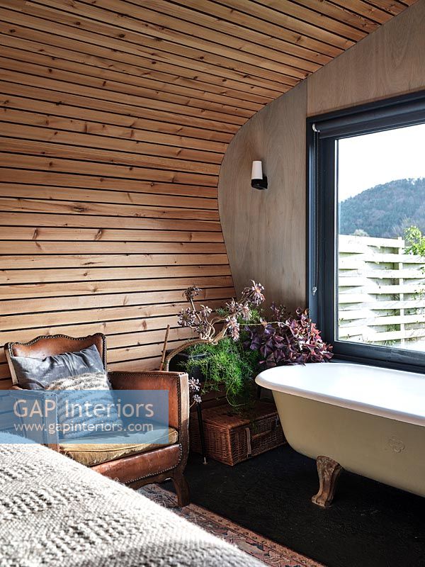 Fauteuil en cuir vintage et baignoire dans une chambre en bois moderne