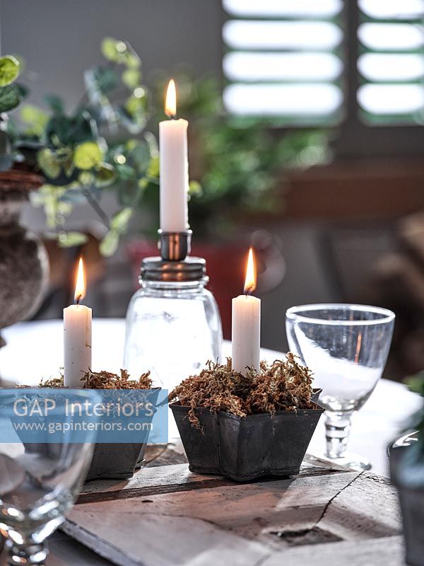 Petites bougies dans des pots en forme d'étoile remplis de mousse sur la table à manger