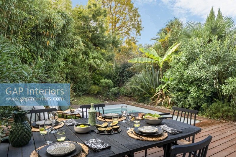 Table à manger en plein air sur la terrasse à côté de la piscine dans un petit jardin