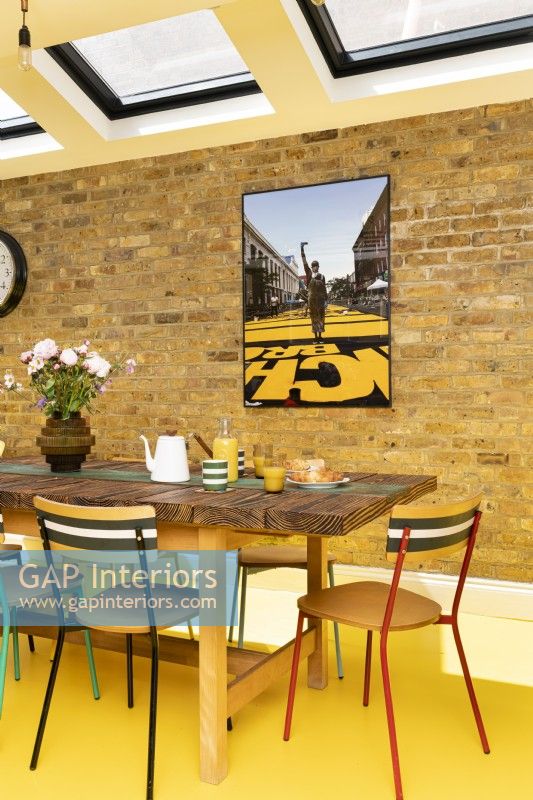 Salle à manger moderne avec briques apparentes, sol en caoutchouc jaune, table et chaises recyclées