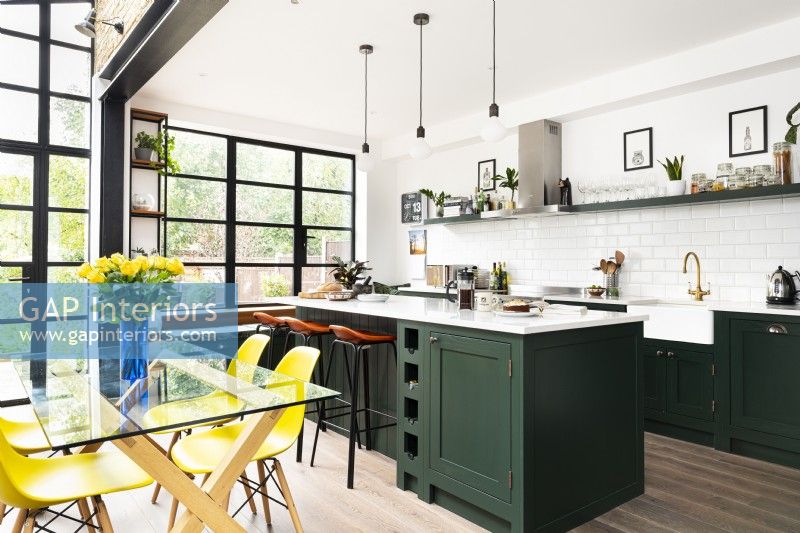 Extension de cuisine contemporaine avec armoires vertes, îlot, fenêtres de style crittall et chaises de salle à manger jaunes