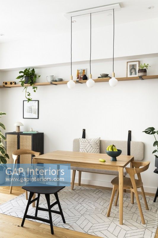 Salle à manger contemporaine minimaliste scandinave avec table en bois, pendentifs, meubles de couleur noir et chêne, étagères ouvertes et banquette