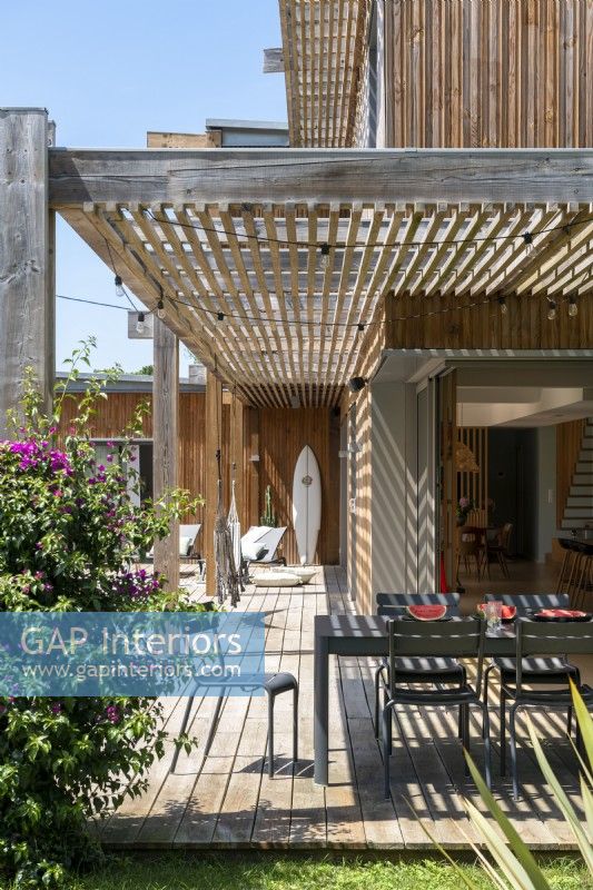 Table à manger ombragée sur une terrasse à côté d'une maison en bois moderne