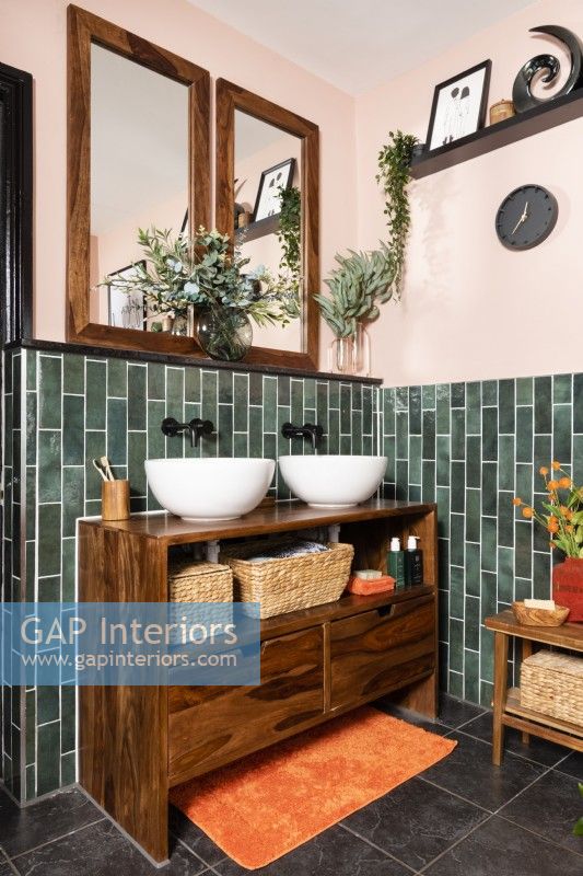 Deux vasques rondes blanches sur une unité en bois dans une salle de bains carrelée de vert