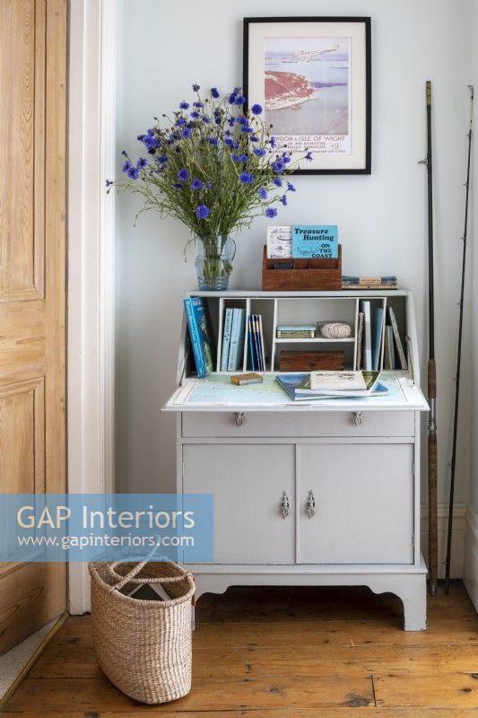 Bureau peint vintage sur le palier, avec de vieux guides, des cannes à pêche et un grand vase de fleurs de centaurée bleue