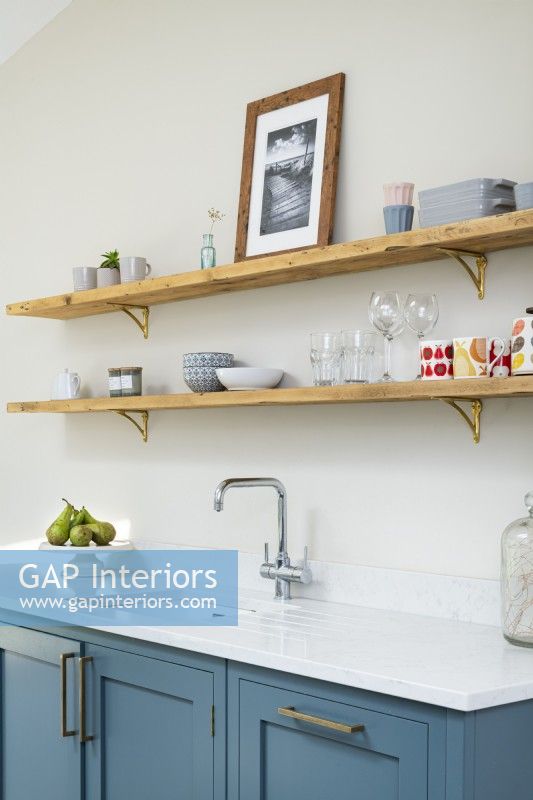 Étagères en bois ouvertes dans une cuisine classique moderne avec supports en laiton, unités bleues, comptoir blanc et robinets.