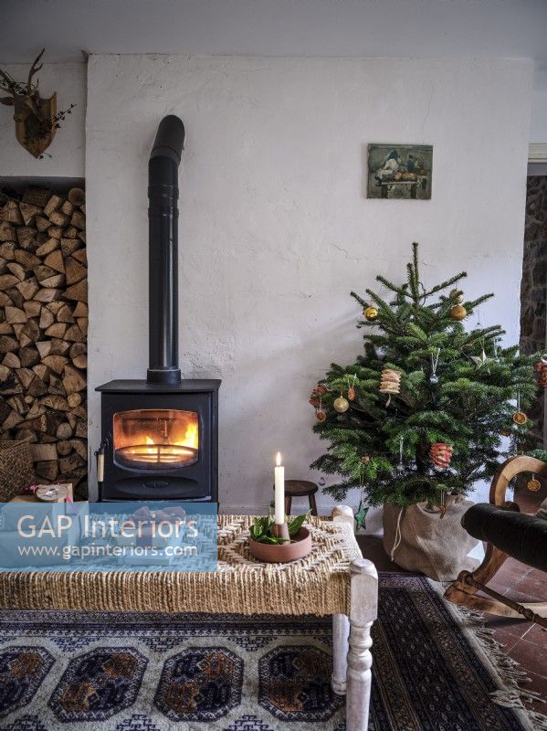 Salon champêtre avec décorations de Noël, bûches empilées et poêle à bois