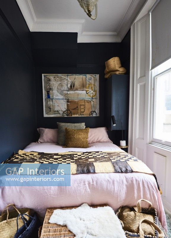 Un lit double dans une petite chambre aux murs peints en noir et aux tissus de style ethnique.