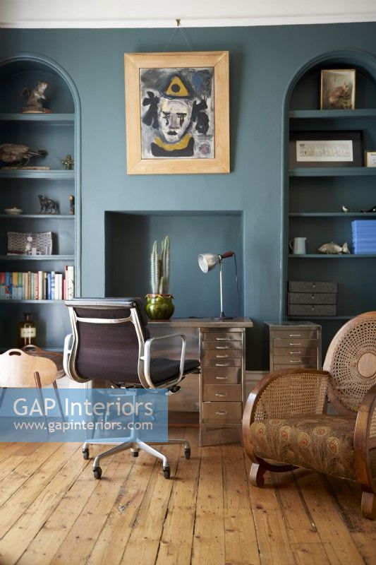 Un bureau et une chaise vintage design contre des murs bleu foncé et des étagères intégrées.