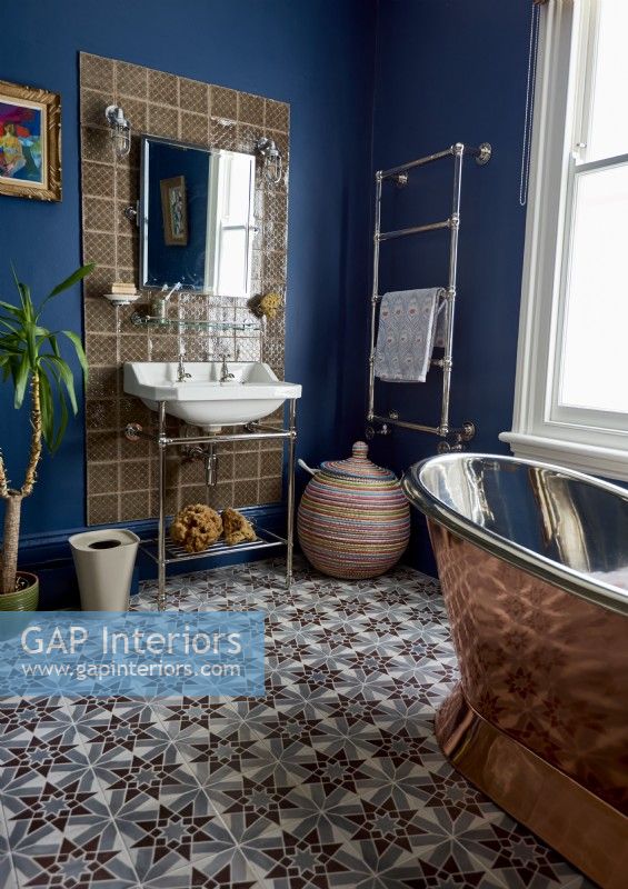 Une salle de bain bleu foncé avec une baignoire autoportante de couleur cuivre et un lavabo de style victorien.