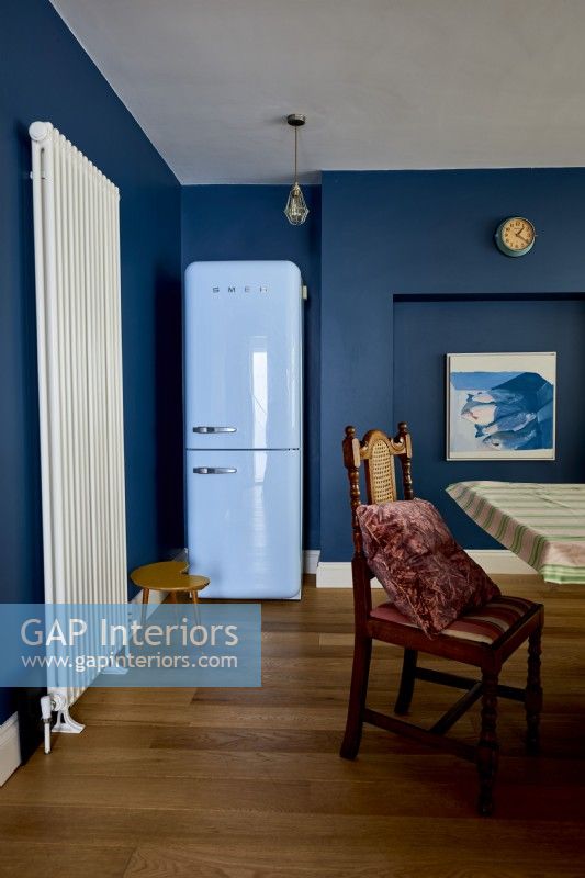 Détail d'une salle à manger montrant un réfrigérateur bleu et un radiateur mural vertical.