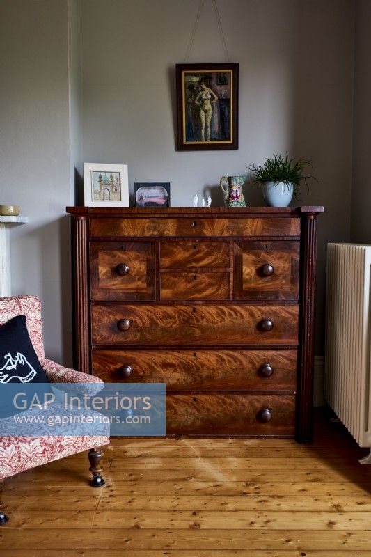 Commode antique dans une chambre à coucher à côté d'une chaise antique recouverte de tissu design William Morris.