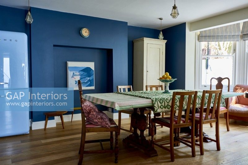 Une salle à manger ouverte, avec une table et des chaises du milieu du siècle, bébé de murs bleu foncé.