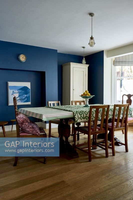 Salle à manger avec des murs peints en bleu foncé et une table et des chaises vintage et anciennes.