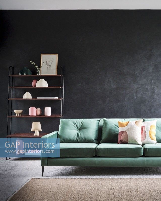 Canapé vert contre un mur gris chiné avec étagères autoportantes