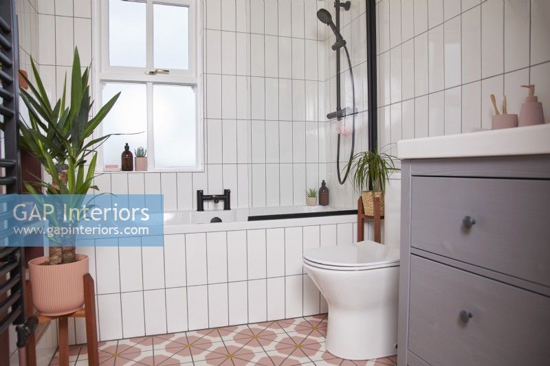 Salle de bain avec sol en vinyle coloré, robinetterie noire, carrelage blanc et meuble sous lavabo gris.