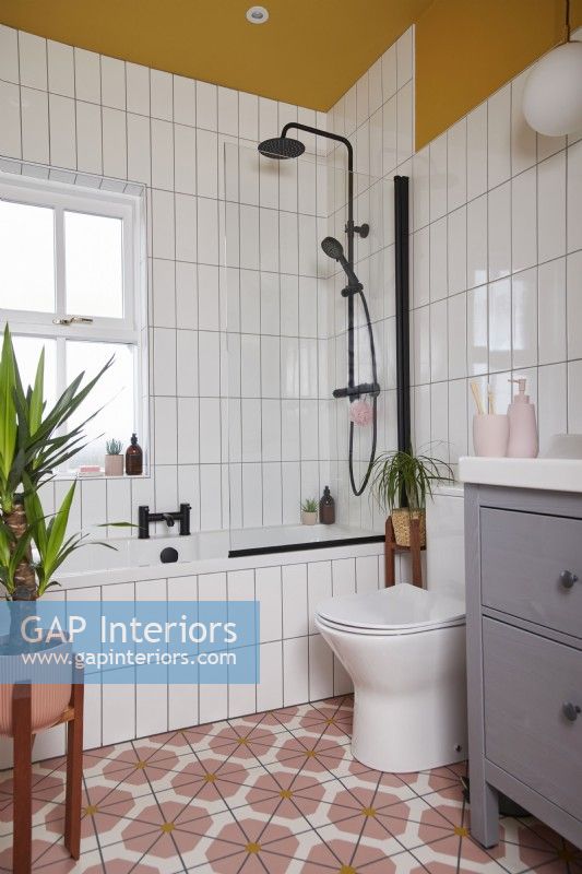 Salle de bain avec sol en vinyle coloré, robinetterie noire, carrelage blanc et murs et plafond peints en jaune.