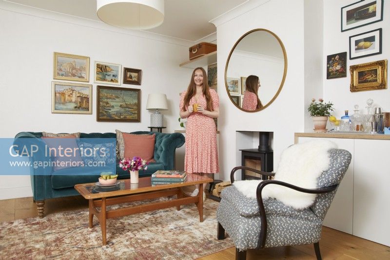 Salon avec un canapé bleu sarcelle, un fauteuil, un poêle à bois et des peintures à l'huile vintage au mur.