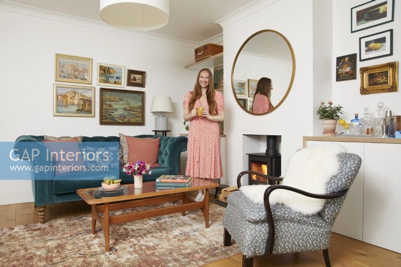 Salon avec un canapé bleu sarcelle, un fauteuil, un poêle à bois et des peintures à l'huile vintage au mur.