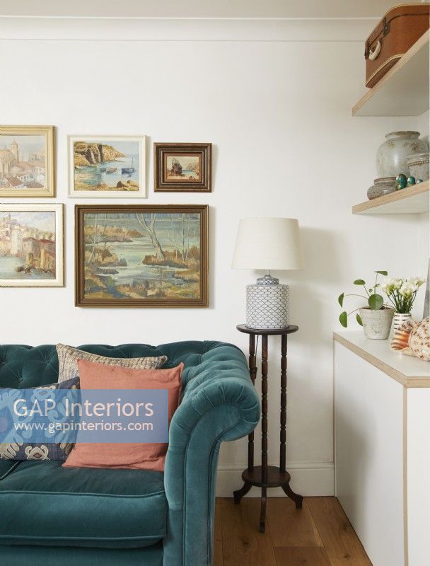 Détail du salon avec un canapé bleu sarcelle, des peintures à l'huile vintage sur le mur et une lampe.