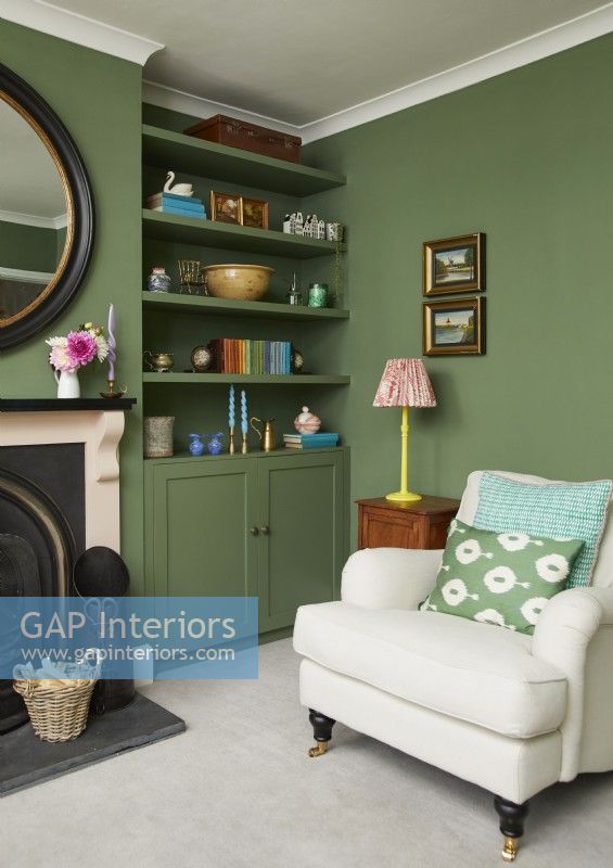 Salon avec fauteuil crème, cheminée, peintures à l'huile vintage et étagères peintes en vert.