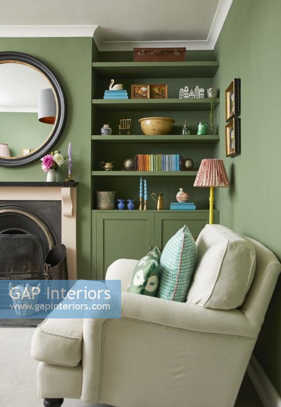 Salon avec fauteuil crème, cheminée, peintures à l'huile vintage et étagères peintes en vert.