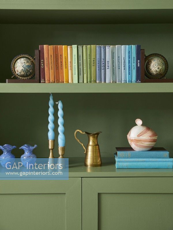 Détail du salon avec étagères peintes en vert avec collection arc-en-ciel de livres et d'ornements.