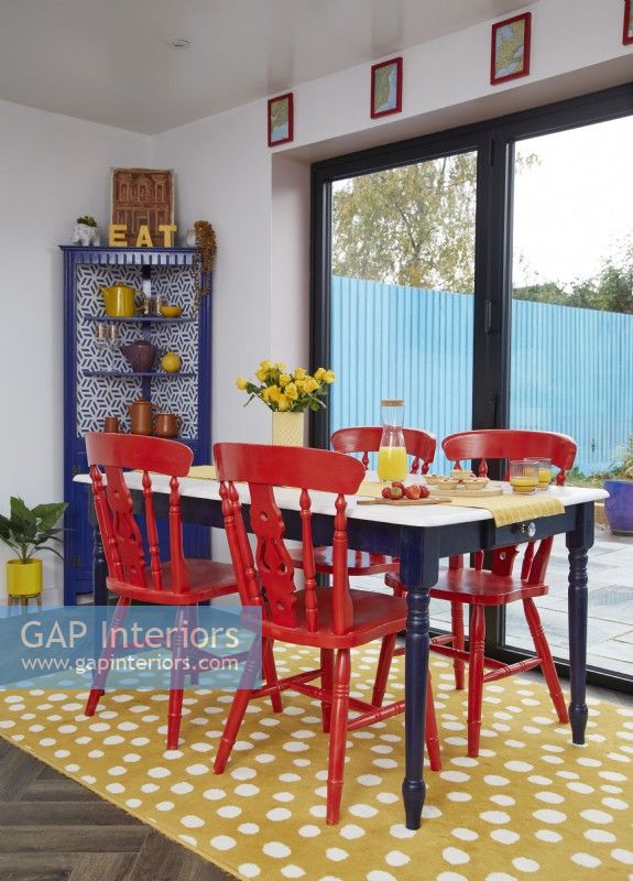 Salle à manger décloisonnée avec des chaises peintes en rouge et un tapis jaune à pois.