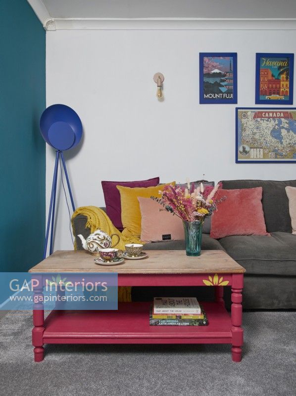 Salon avec un grand canapé gris, un mur peint en bleu sarcelle et une table basse rose.