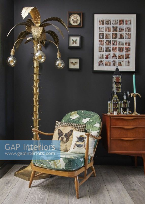 Détail du salon avec un fauteuil rétro Ercol, un lampadaire palmier et un buffet vintage en bois.