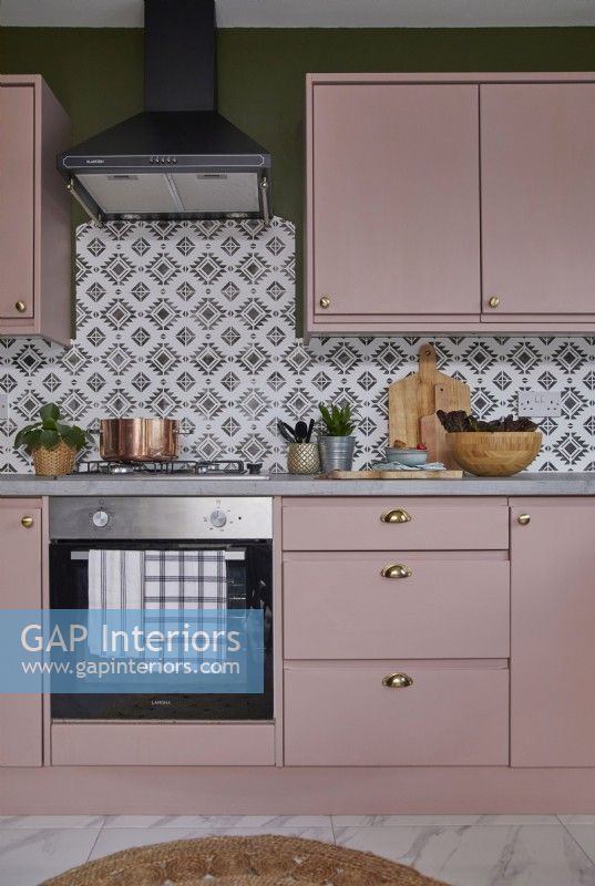 Détail de la cuisine avec four, armoires roses et carreaux à motifs.