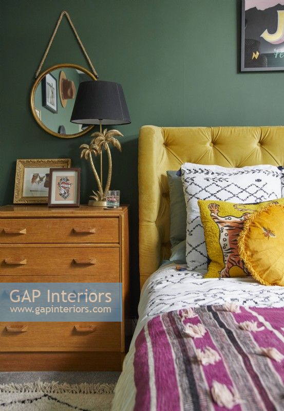 Détail de la chambre montrant un lit double jaune, des tiroirs vintage en bois et des murs peints en vert.