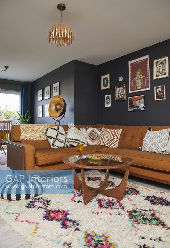 Salon avec un canapé en cuir marron, une table basse vintage, une galerie d'estampes encadrées et des murs peints en bleu foncé.