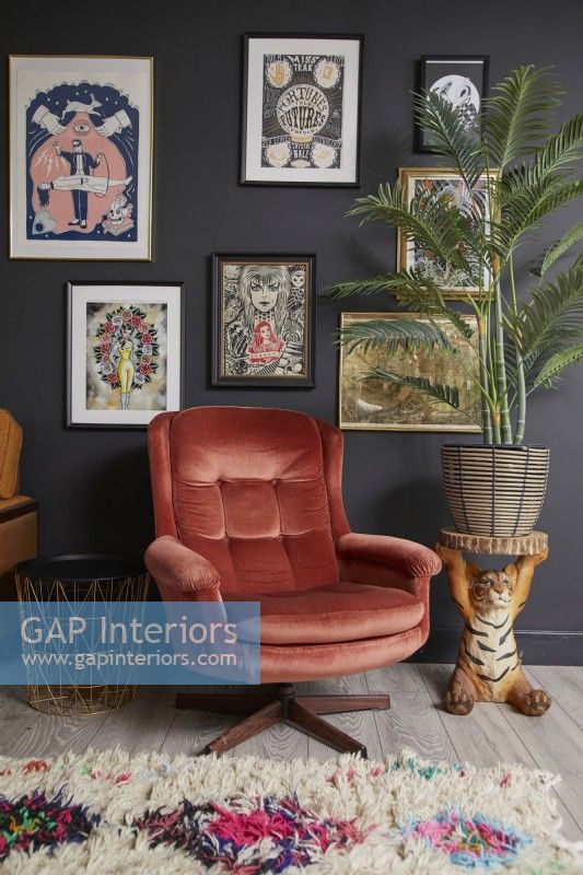 Détail du salon avec un fauteuil rétro, une table de plantes tigrées et un mur de galerie d'illustrations.