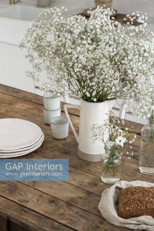 Fleurs blanches et verseuse sur table de cuisine en bois de campagne