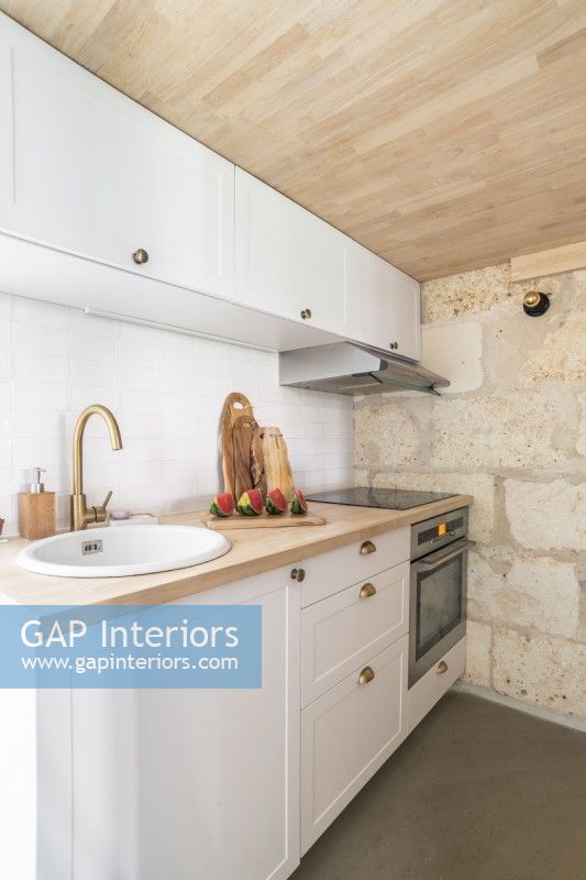 Petite cuisine moderne avec mur en pierres apparentes et plafond en bois