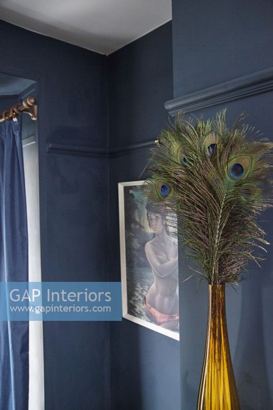 Détail du salon montrant des plumes de paon décoratives dans un vase, des œuvres d'art rétro et des murs peints en bleu marine.
