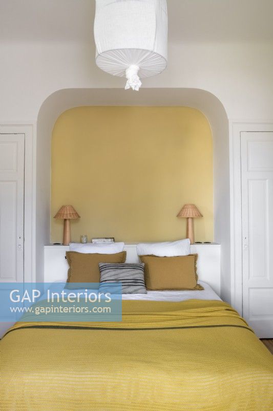 Alcôve peinte en jaune au-dessus du lit dans la chambre blanche
