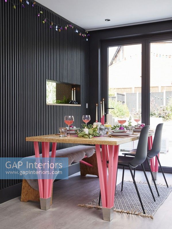 Salle à manger à aire ouverte avec boiseries noires. Table à manger en OSB avec pieds en néon rose et décor de table de Noël.