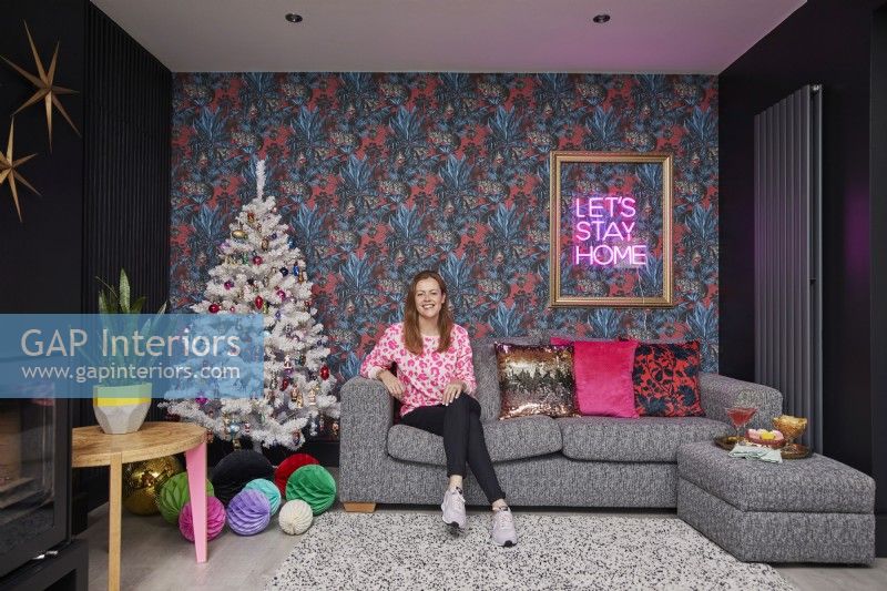 Salon ouvert décoré pour Noël. Canapé confortable avec coussins colorés, papier peint à motifs, murs noirs et poêle à bois.