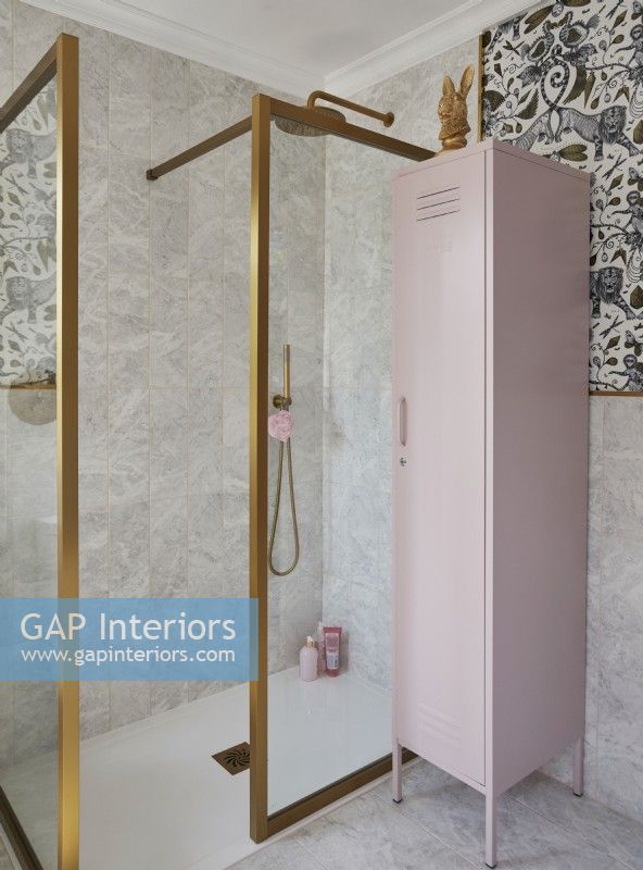 Salle de bain avec papier peint à motifs, cabine de douche à cadre doré et casier de rangement rose.