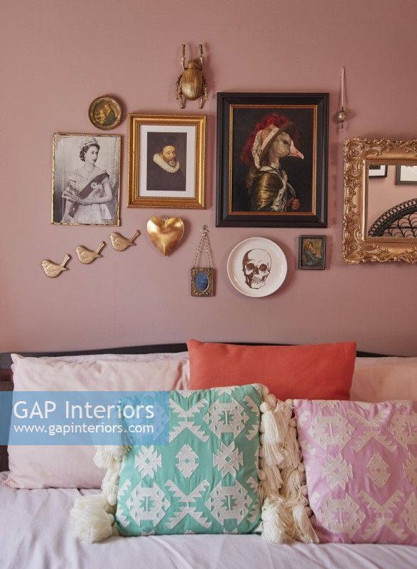 Détail de la chambre montrant un lit avec des coussins texturés et un mur de galerie rose avec des accents dorés.