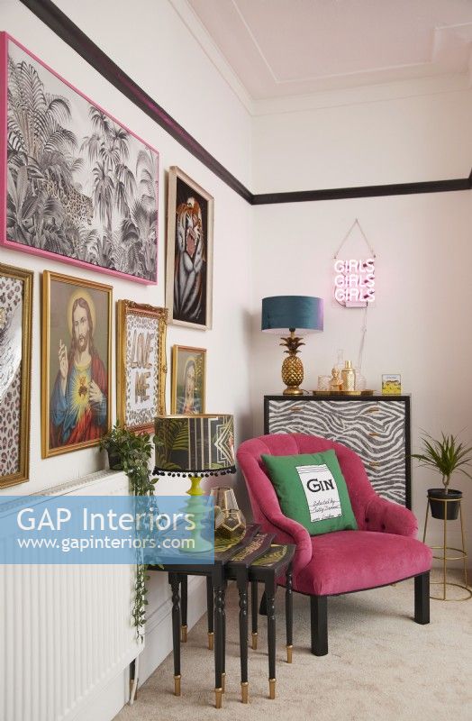 Colourful living room detail with a pink armchair, nest of side tables a gallery wall.
