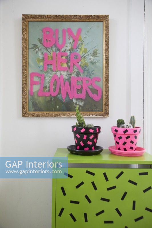Détail du hall d'entrée avec imprimé 'Buy her flowers', pots de plantes décorés de washi tape et placard.