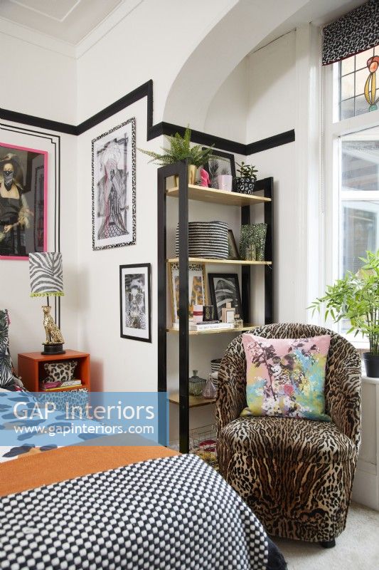 Chambre avec un effet de faux lambris noir (avec du ruban washi noir), des œuvres d'art encadrées et un fauteuil à imprimé animalier.