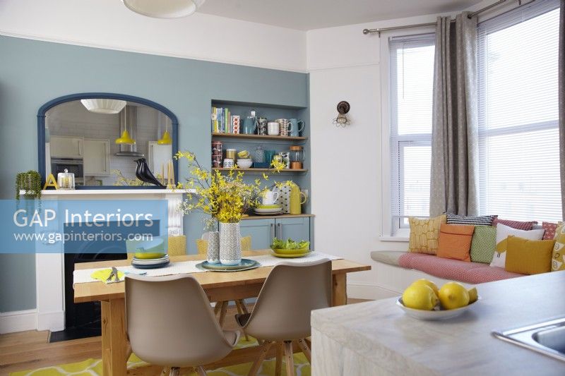 Open plan kitchen-diner with blue walls, a victorian fireplace and window seating.
