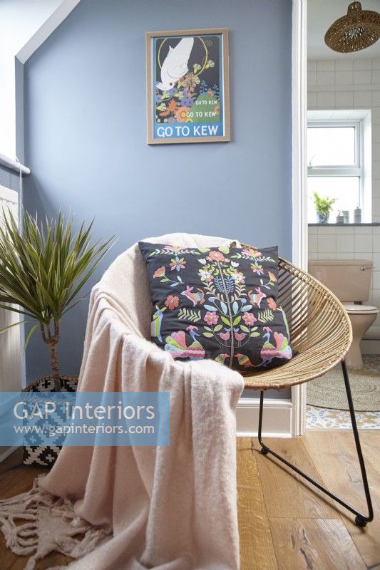 Détail de la chambre montrant une chaise en osier, des œuvres d'art sur des murs peints en bleu.